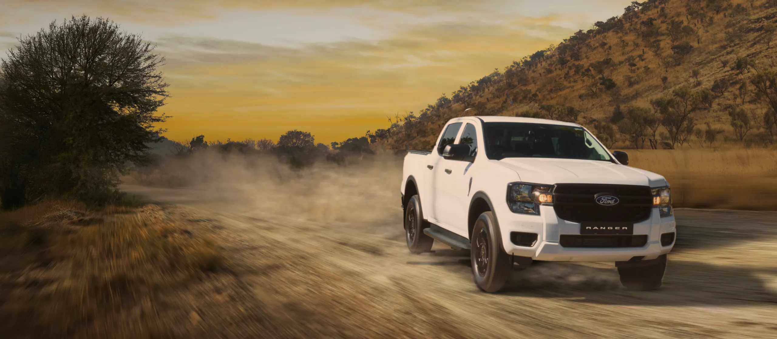 White Ford Ranger XL Double Cab driving on a dusty gravel road in the bushveld at sunset